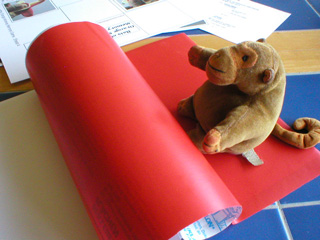 Mr Monkey rolling red sticky-back plastic onto the back of a sheet of cards