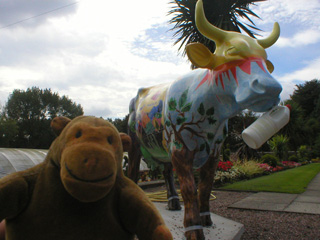 Mr Monkey in front of a cow painted with trees for legs, and a sun on its head