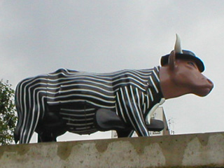 A cow in a pin-striped suit and fedora, carrying a violin case