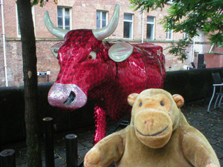 Mr Monkey in front of a cow covered in a deep red pattern