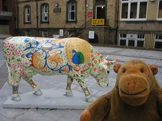 Mr Monkey in front of a cow covered in small flowers, ornate swirls, and a peacock