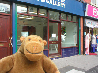 Mr Monkey outside a gallery with a cow in the window
