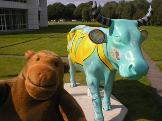 Mr Monkey in front of a turquoise cow with yellowing writing on it