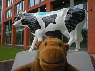 Mr Monkey in front of a cow with a poem written on its black patches