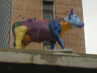 A cow made of coloured pieces stitched together with large pins sticking in it