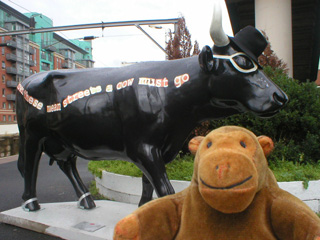 Mr Monkey in front of a black cow with 'Down these mean streets a cow must go' on its side