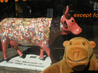 Mr Monkey looking through a window at a brick red cow covered in faces