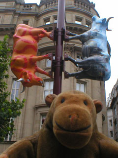 Mr Monkey in front of two cows fixed to a lamp post