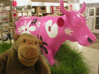 Mr Monkey in front of a pink cow covered in large white, red, and purple flowers