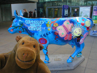 Mr Monkey in front of a blue cow decorated with butterflies and other creatures