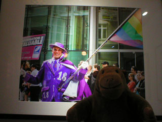 Mr Monkey looking at a picture of a Pride marcher dressed in purple