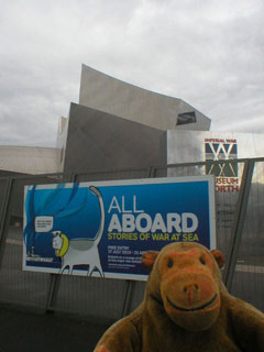 Mr Monkey examining the exhibition poster on the fence around the museum