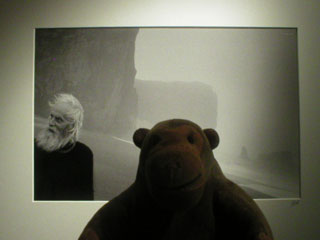 Mr Monkey looking at a photo of a bearded  man on a beach by Ragnar Axelsson