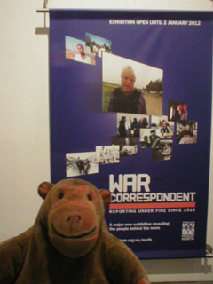 Mr Monkey looking at the poster outside the War Correspondent exhibition