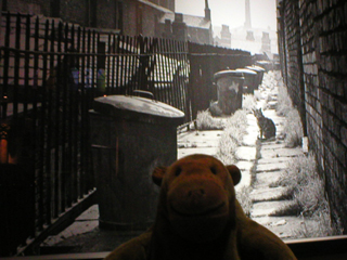 Mr Monkey looking at a photo by Sefton Samuels of a Salford back street in 1962