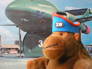 Monkey in his Thunderbirds hat, standing on a runway next to Thunderbird 2