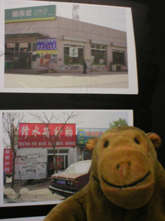 Mr Monkey in front of some pictures of Ban Zheng numbers on rough looking buildings