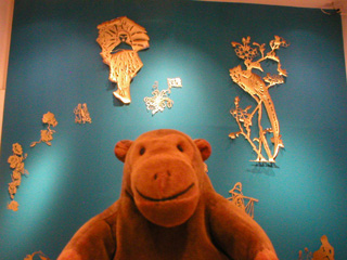 Mr Monkey looking at a wall of cutouts by Karen Tam