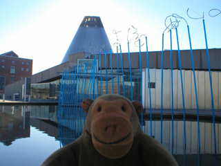 Mr Monkey looking at blue glass poles in a pool outside the museum