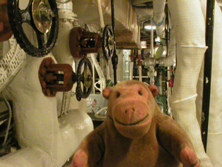 Mr Monkey looking at pipes and control wheels in the forward boiler room