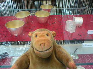 Mr Monkey looking at small gold plate bowls and napkin rings by Shimara Carlow