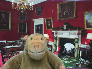Mr Monkey in front of a picture of the saloon of Fairfax House