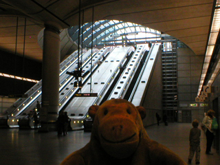 Mr Monkey looking at the escalators out of Canary Wharf tube station