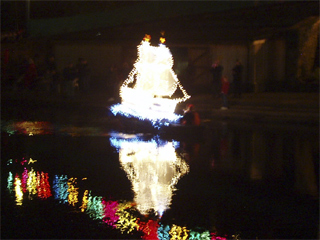 The illuminated galleon being rowed past the boathouse
