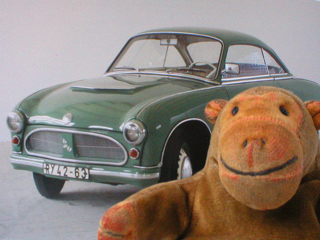 Mr Monkey in front of a photo of a P70 coupé
