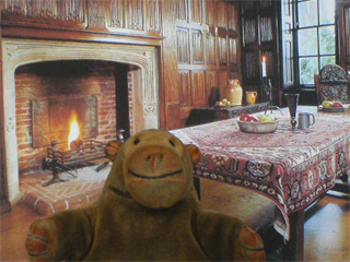 Mr Monkey in front of a postcard of the Linenfold Parlour of Sutton House