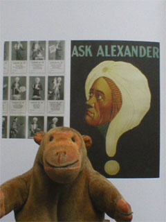 Mr Monkey in front of a picture of an Ask Alexander poster