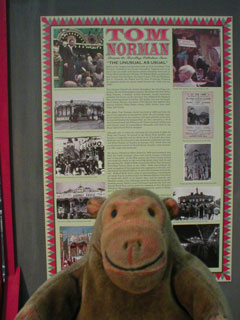 Mr Monkey reading an information panel about Tom Norman