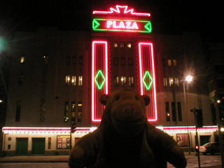 Mr Monkey approaching the illuminated cinema in the evening