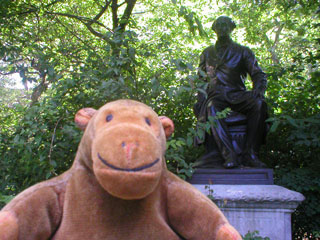 Mr Monkey in front of a statue of John Stuart Mill