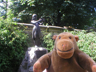 Mr Monkey in front of a statue of a girl holding a bowl