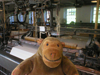 Mr Monkey in front of a row of looms weaving