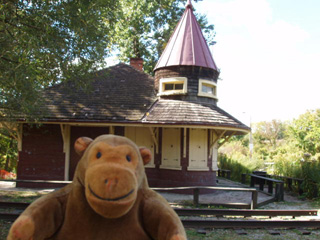 Mr Monkey in front of a maroon and cream building with a small tower