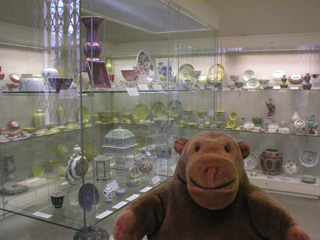 Mr Monkey in front of a cabinet of variously coloured ceramics