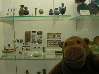 Mr Monkey looking at a cabinet full of small ancient glass vessels