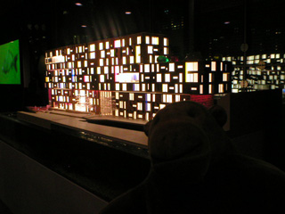 Mr Monkey in the dark in front of a model of a housing block