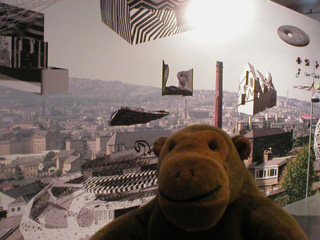 Mr Monkey in front of a town with odd objects floating above it