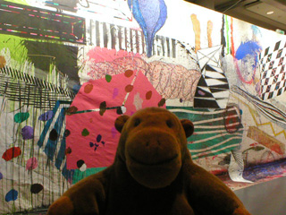Mr Monkey in front of a brightly and randomly decorated wall