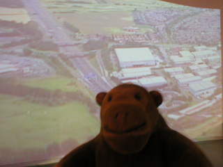 Mr Monkey in front of a view of the M62 from the air