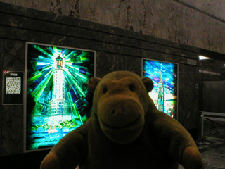 Mr Monkey in front of illuminated panels showing the wonders of the world