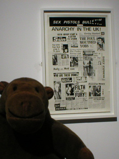 Mr Monkey with a poster made up of press reports about the Sex Pistols