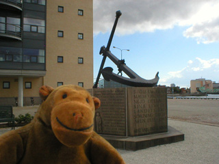 Mr Monkey in front of an anchor on a plinth