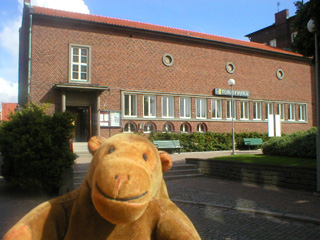 Mr Monkey outside a plain brick tourist office