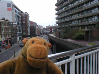 Mr Monkey looking down onto Aldergate Street from a highwalk at the Barbican