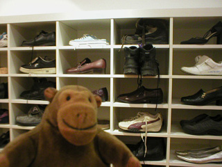 Mr Monkey in front of a shelf of shoes, including Mr Rik's boots