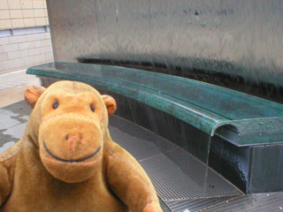 Mr Monkey looking at a bench-like sculpture cascading with water